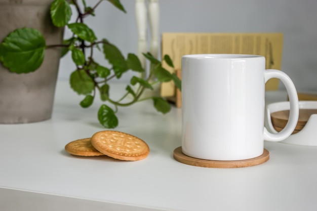 Taza de desayuno con galletas junto a una planta en una mesa blanca