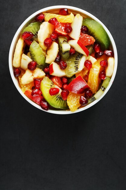 Taza de ensalada de frutas frescas hecha de frutas jugosas sobre una superficie negra. Espacio libre para texto. Rodajas de frutas frescas, jugosas y saludables para una dieta saludable.