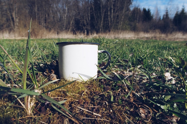 Taza de esmalte blanco sobre suelo de hierba de bosque