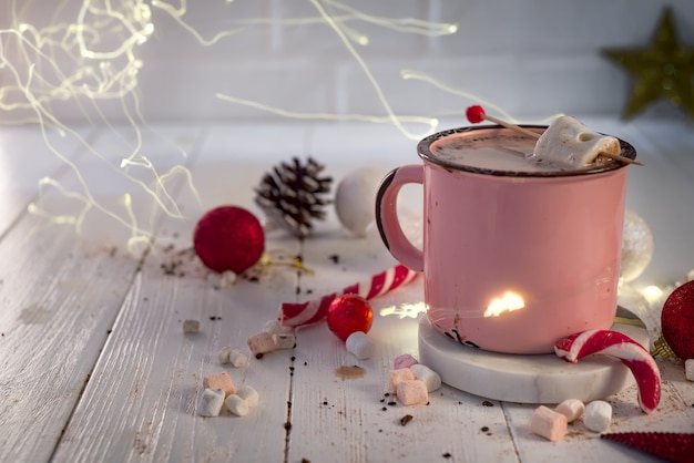 Taza de esmalte de chocolate caliente con malvaviscos y bastones de caramelo con hermosas luces de Navidad