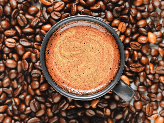 Taza de espresso con espuma entre granos de café tostados