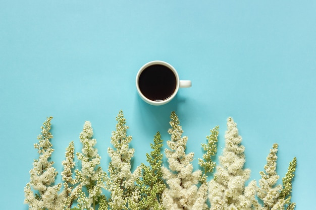 Taza de flores blancas de la ramita floreciente del café y de la fila en fondo del papel azul