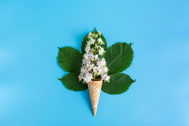 Taza de gofre crujiente dulce con flor de castaño y hojas sobre fondo azul.