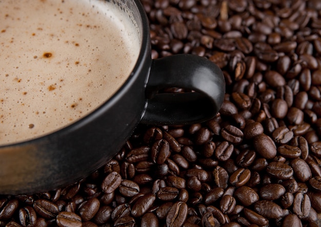 Taza grande con capuchino caliente con granos de café sobre tabla de madera