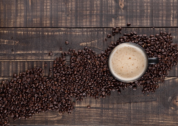 Taza grande con capuchino caliente con granos de café sobre tabla de madera