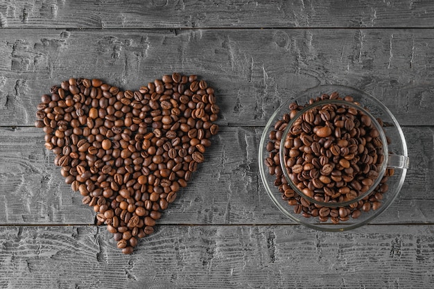 Una taza de granos de café y un corazón forrado con granos de café sobre una mesa de madera negra. La vista desde la cima. Granos para la preparación de la bebida popular. La vista desde la cima.