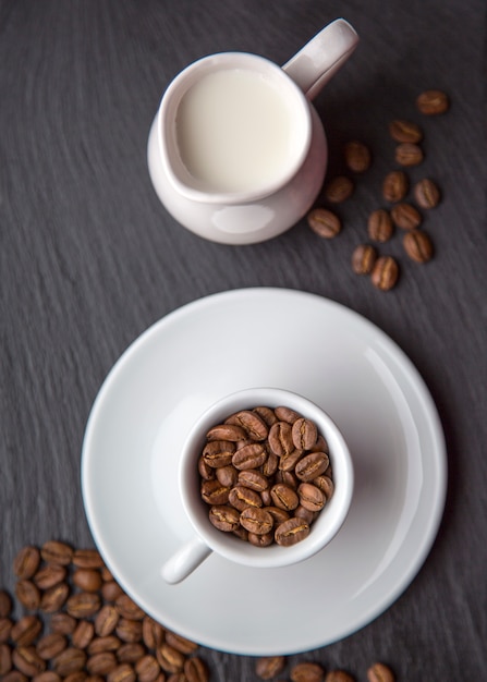 Foto taza de granos de café con leche sobre fondo negro gris vista superior luz natural enfoque selectivo