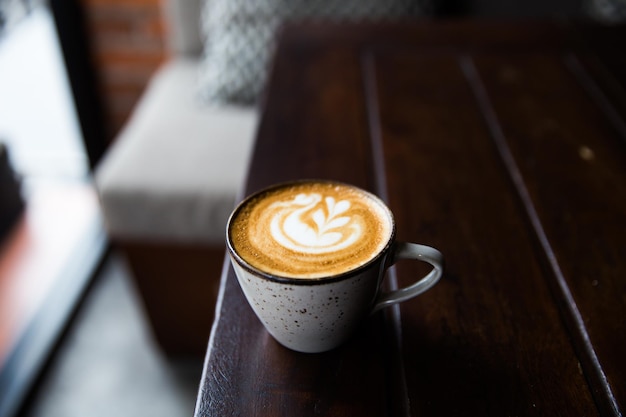 Taza gris de capuchino caliente sobre fondo de escritorio de madera