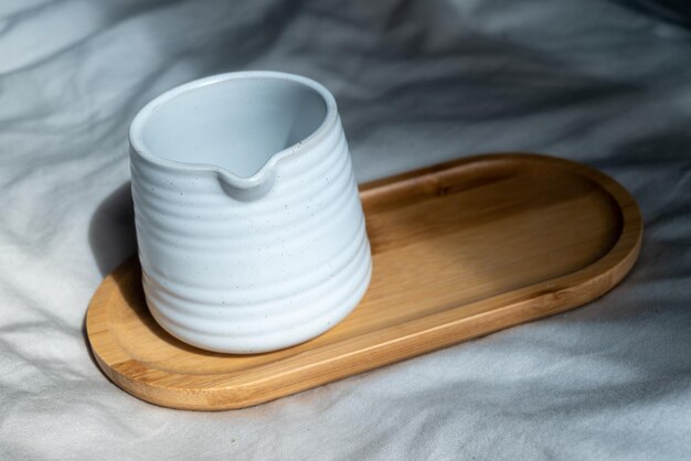 Taza hecha de arcilla blanca o taza de cerámica en la placa de madera, fondo de tela y luz natural