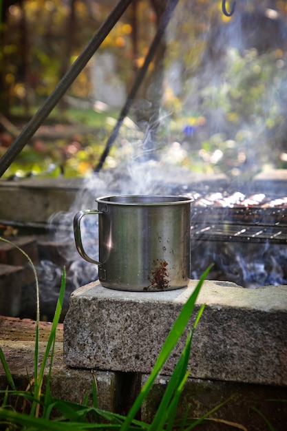 Taza de hierro con bebida caliente cerca del fuego