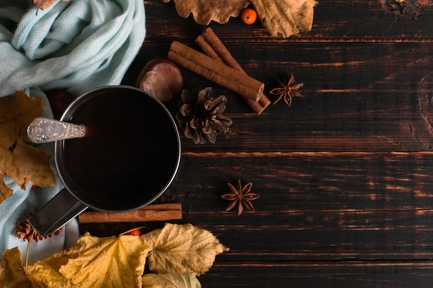 Taza de hierro con café negro, especias, sobre un fondo de una bufanda, hojas secas sobre una mesa de madera. Humor de otoño, una bebida caliente. copyspace