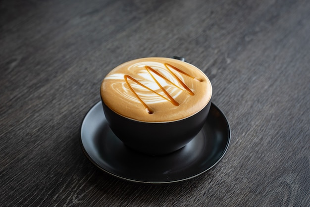 Una taza de Hot Caramel Macchiato sobre escritorio de madera