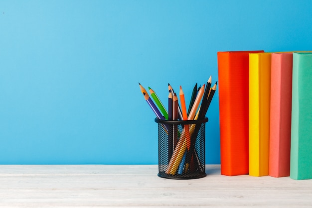 Taza de lápices de colores y pila de libros sobre la mesa