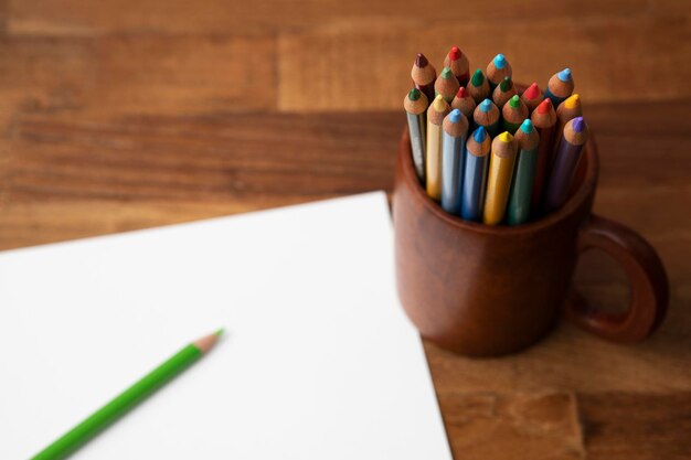 Foto una taza de lápices de colores se sienta en una mesa de madera junto a una hoja de papel blanca.