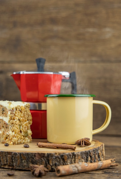 Una taza de lata amarilla de café caliente con cafetera italiana (Moka) y pastel en la mesa de madera.