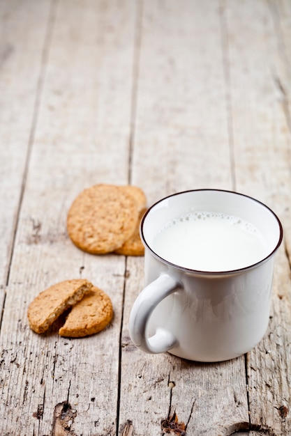 Taza de leche y algunas galletas de avena recién horneadas en una mesa de madera rústica