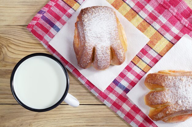 Taza de leche y bollos con mermelada para el desayuno en la mesa de madera con mantel, vista superior