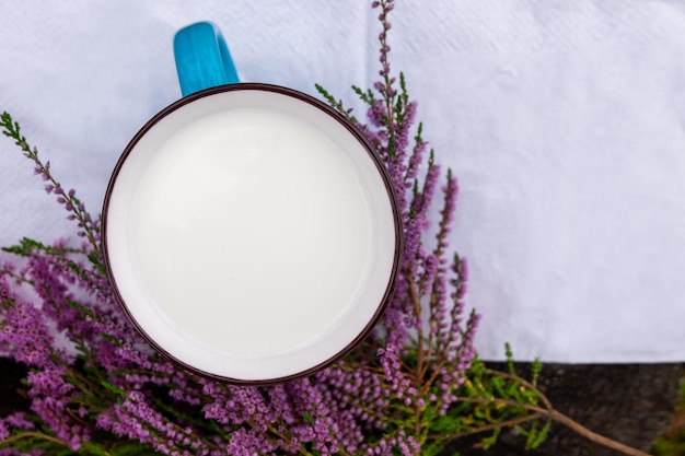 Una taza de leche y flores de brezo en una mesa de madera