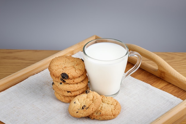 Taza de leche y galletas con pasas en una bandeja de madera