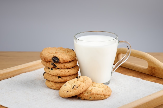 Taza de leche y galletas con pasas en una bandeja de madera