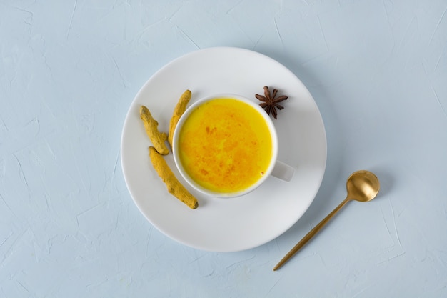 Taza de leche con leche de cúrcuma dorada ayurvédica con cúrcuma en polvo en azul. Vista desde arriba.