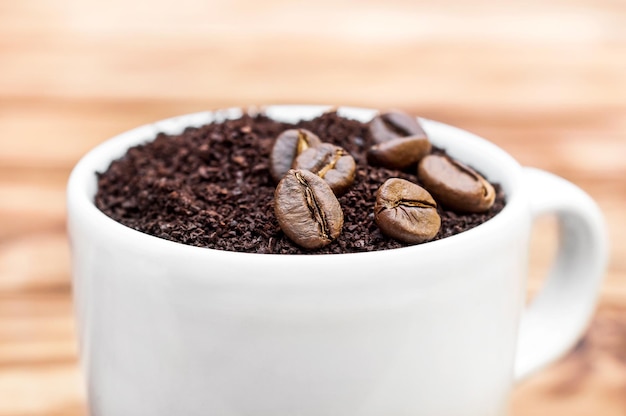 Taza llena de café molido con granos de café Cerrar