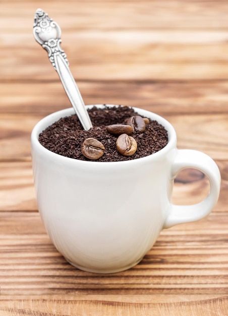 Foto taza llena de café molido con granos de café y cuchara sobre mesa de madera