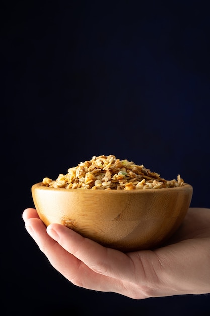 Taza llena de muesli en mano sobre fondo negro