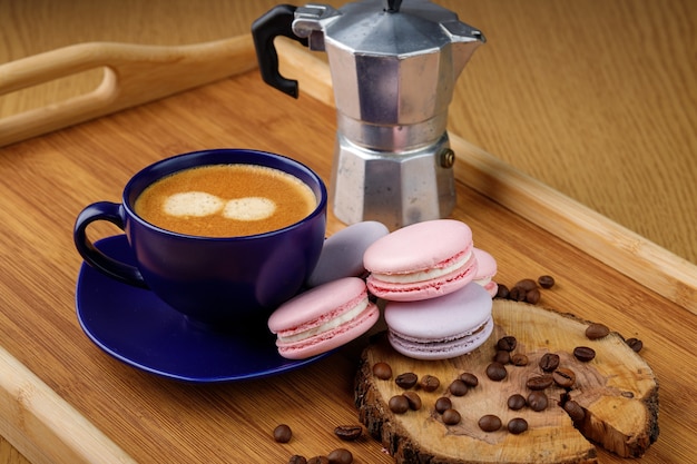 Foto taza de macarrones de café y granos de café en un plato y cafetera géiser en una bandeja de madera