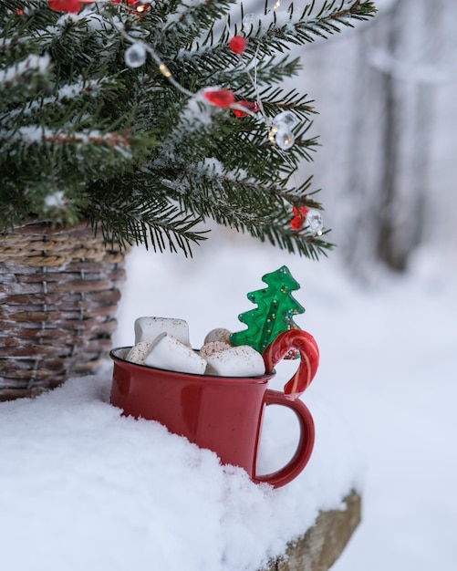 Taza con malvaviscos y dulces navideños en la nieve en el parque de invierno