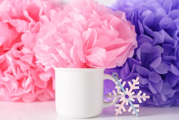 Taza de maqueta de navidad blanca sobre fondo de flores de papel lila y rosa