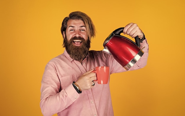 Una taza más brutal hombre guapo con bigote beber té hombre maduro marido sostener hervidor eléctrico tecnología moderna en la vida barbudo hipster usar electrodomésticos concepto de cocina