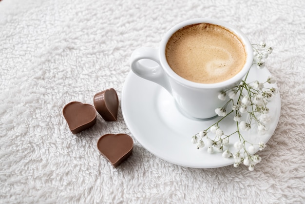 Taza matutina de café expreso fuerte con chocolates en forma de corazón servido en la cama. Celebración del día de San Valentín