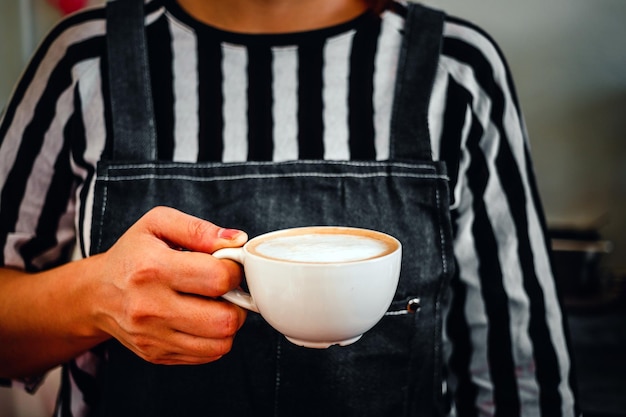 Foto una taza de menú de capuchino de café listo para servir en la mano mujer barista en la cafetería