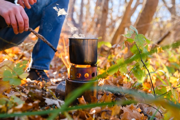 Taza de metal en un fuego abierto en el bosque Un turista calienta agua en una taza de metal en un incendio en un bosque de otoño