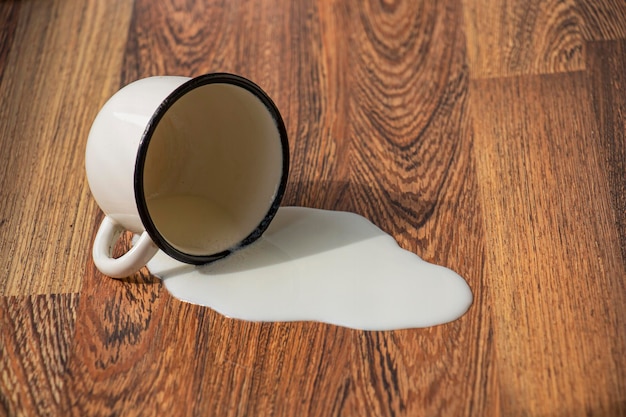 Taza de metal con leche cayó al suelo mancha de leche derramada en el suelo de madera