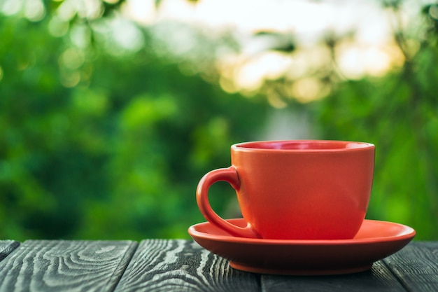 Taza naranja de café caliente en una mesa de madera en un jardín verde por la mañana o por la noche