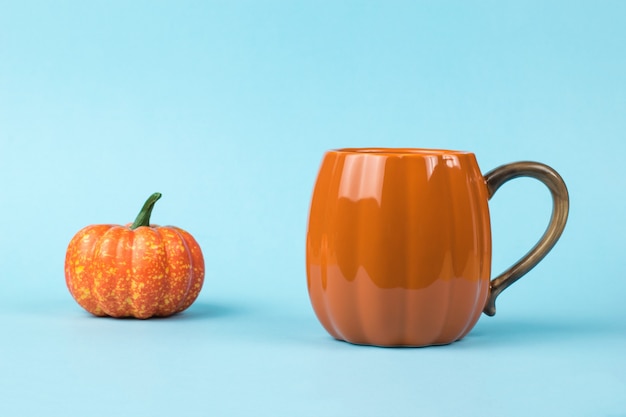 Foto una taza naranja y una figura de calabaza sobre un fondo azul. estilo calabaza.