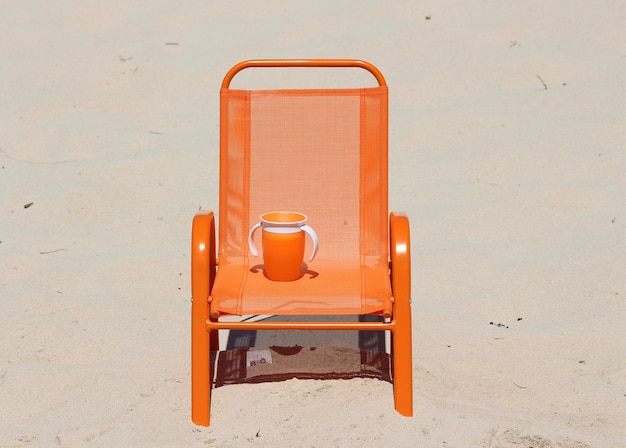 Foto taza naranja y silla en la playa durante un día soleado