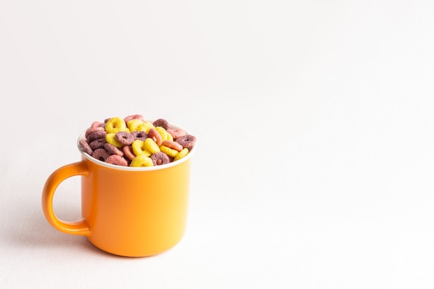 Taza naranja sobre fondo blanco llena de coloridos anillos de cereales con espacio de copia