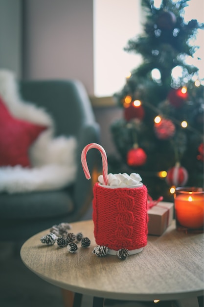 Taza de Navidad de cacao con malvaviscos, sobre una mesa de madera con el telón de fondo de un árbol de Navidad. Estado de ánimo de año nuevo.