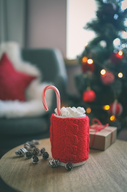 Taza de Navidad de cacao con malvaviscos, sobre una mesa de madera con el telón de fondo de un árbol de Navidad. Estado de ánimo de año nuevo.