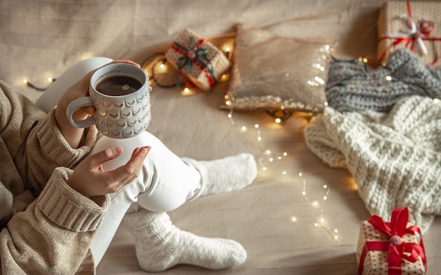 Taza de Navidad hermosa en manos femeninas en la pared borrosa de decoración acogedora.