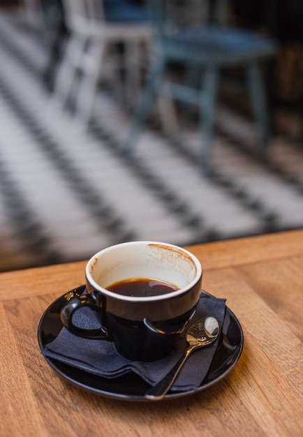 Una taza negra de café espresso medio lleno en la mesa de madera por la mañana