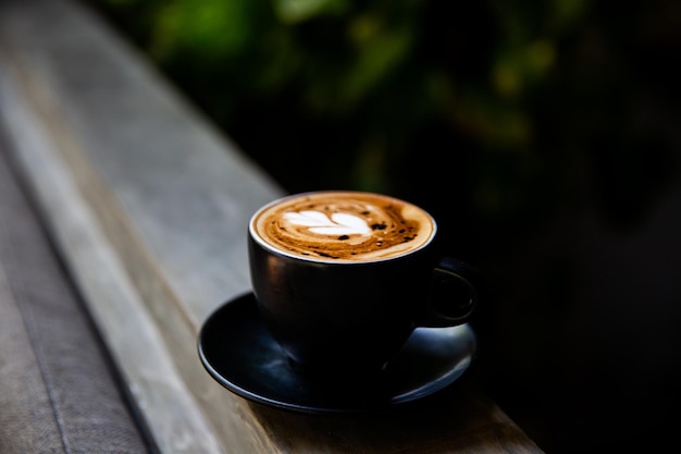 Taza negra de capuchino con arte latte en platillo sobre fondo de madera