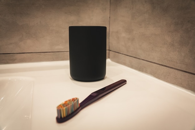 Foto taza negra para un cepillo de dientes en el fondo de un baño gris