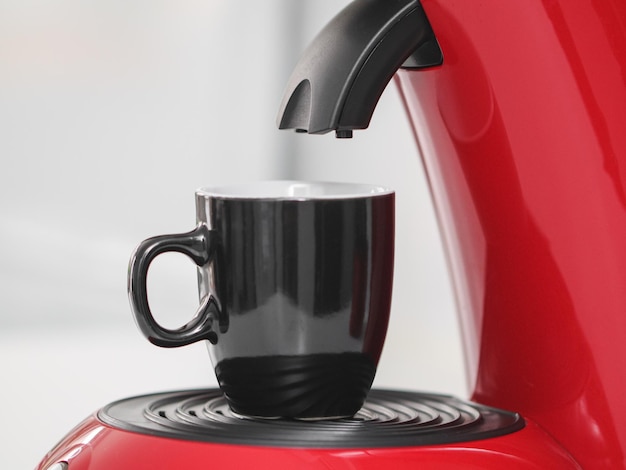 Una taza negra se encuentra sobre una cafetera roja en un armario de cocina con luz de fondo borrosa