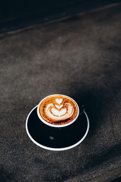 Taza negra de sabroso capuchino con arte latte sobre fondo de hormigón gris en el café