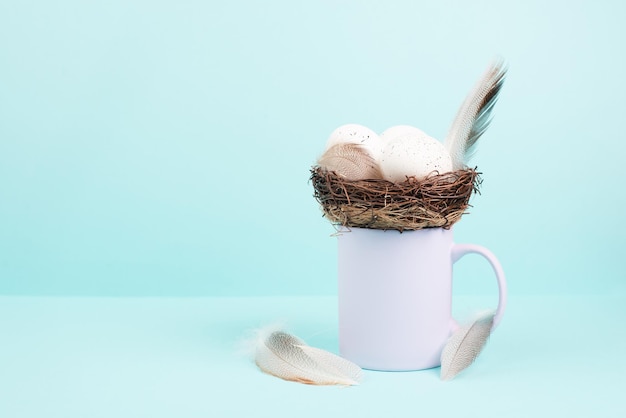 Taza o taza con un nido de huevos de pascua y plumas de pájaro, tarjeta de felicitación de vacaciones de primavera