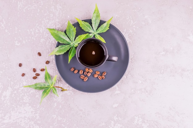 Una taza oscura con café aromático y hojas de connabis en un plato se alza sobre un fondo de hormigón gris. El concepto de café matutino para obtener energía.